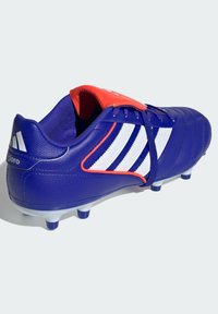 Botas de fútbol sintéticas azules con acentos rojos, diseño de tres rayas blancas, superficie texturizada y tachuelas de goma para tracción.