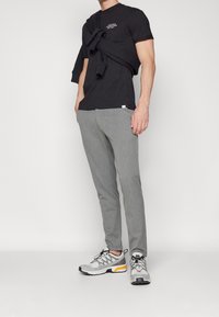 Zwarte katoenen T-shirt met korte mouwen, grijze getailleerde broek met textuur en grijze sneakers met oranje accenten. Trui om de schouders gebonden.