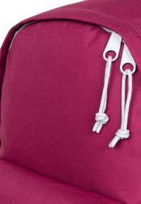 Rosa tygryggsäck med vita dragkedjor och flätade snörningar. Texturen är slät, med en rundad form och vadderad struktur.