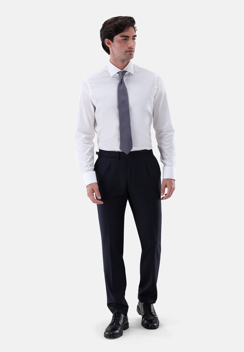 Weißes Hemd, graue gemusterte Krawatte, marineblaue Hose, schwarze Schnürschuhe. Glatter Stoff, maßgeschneiderte Passform, geknöpfte Manschetten und sichtbare Gürtelschlaufen.