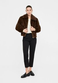 Chaqueta marrón de piel sintética con un amplio cuello, cierre de cremallera y acabado texturizado, combinada con pantalones negros a medida y mocasines negros.