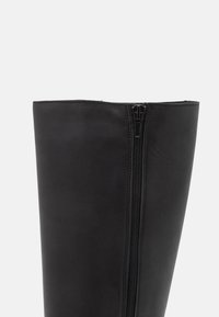 Czarny skórzany wysokiego buta za kolano z bocznym zamkiem błyskawicznym, gładką fakturą i przemyślaną konstrukcją z przeszyciami jako akcentami.