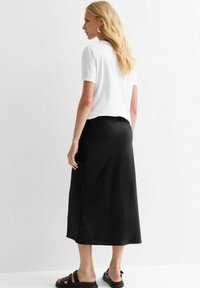 Svart satin midi kjol med en slät textur, sidoöppning och en lös passform, kombinerad med en vit kortärmad topp och svarta sandaler.