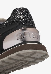 Zapatilla negra con una parte superior brillante en negro y un talón metálico plateado. Suela de goma marrón con un exterior texturizado para mayor agarre y durabilidad.