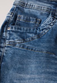 Jeans aus Denim mit hellblauer Waschung, ausgestattet mit einer Vordertasche und kontrastierenden gelben Nähten entlang der Nähte und Taschenkanten.