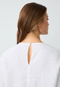 Camicia bianca in lino con un'apertura a keyhole sulla schiena, realizzata in un tessuto morbido e strutturato, con maniche ampie.