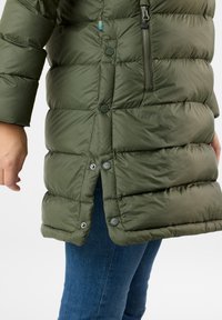 Olive green puffer coat with a zippered pocket, snap buttons, and quilted texture. Features a high collar and a fitted design at the hem.
