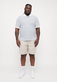 Polo de manga curta em branco com riscas azuis-marinho, combinado com calções cargo bege, ténis brancos e meias brancas até ao tornozelo.