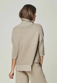 Beige geripptes Strickpullover mit Stehkragen und kurzen Ärmeln, mit lockerer Passform und seitlichen Schlitzen am Saum. Weiches, strukturiertes Material.