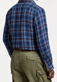 Camicia in flanella a quadri blu e navy con maniche lunghe, texture morbida e polsini con bottoni, abbinata a pantaloni cargo verde oliva.