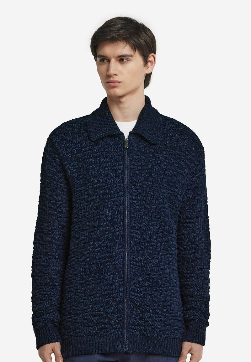 Marinblå stickad zip-sweater med ett texturerat mönster, krage och ribbade ärmslut. Tillverkad av mjukt, varmt material.