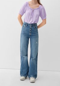 Lilac puff-sleeve top with front tie detail, paired with high-waisted light blue baggy jeans featuring button closure and distressed accents.