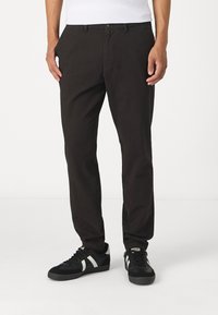 Svart, slim-fit bukser laget av teksturert bomull, med beltehemper og en frontlomme. Bært med svarte joggesko og hvite detaljer.