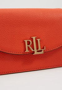 Czerwona, teksturowana skórzana torba z złotym logo "RLL", wyposażona w klapę zapięcia oraz subtelne przeszycia wzdłuż krawędzi.