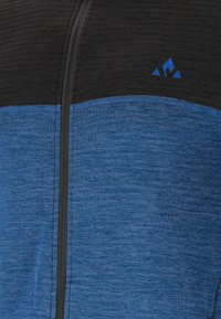 Blå och svart jacka med dragkedja. Texturerat blått tyg med en slät svart övre del. Har en blå logotyp på bröstet.