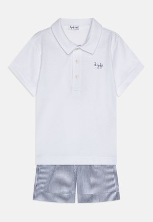 Camisa polo blanca con cuello y tres botones, que presenta un logo en azul marino. Combinada con pantalones cortos a rayas en azul marino y blanco.
