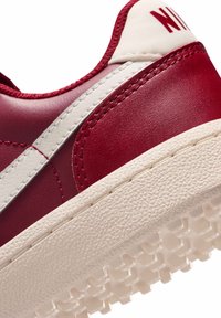 Rode leren sneaker met witte accenten, een gestructureerde crèmekleurige rubberen zool en zichtbare stiksel details. Voorzien van een logo op de tong en zijkant.