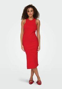 Abito midi rosso a coste con design senza maniche, caratterizzato da una silhouette aderente e una texture liscia. Indossato con ballerine rosse a pois.