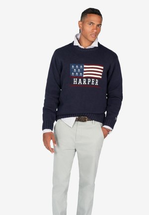 Suéter de punto azul marino con un diseño de la bandera americana y la palabra "HARPER" en blanco, combinado con pantalones claros.