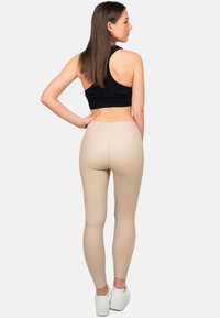 Top corto nero e leggings beige visti da dietro, con una texture liscia e un design snello, accompagnati da calzature bianche.