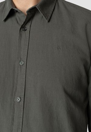 Camisa de botones gris oscuro hecha de tela texturizada. Cuenta con cuello clásico, botones frontales y un logo bordado sutil en el pecho.