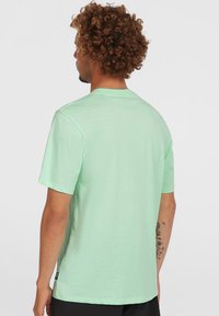 Camiseta de manga corta verde menta hecha de tela suave; presenta un escote redondo y un dobladillo recto con una pequeña etiqueta de logo en el costado.