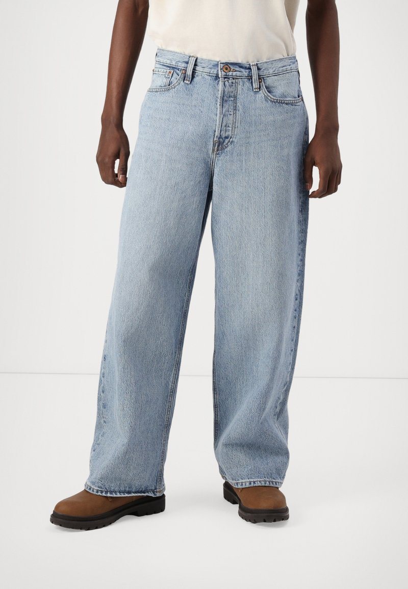 Light blue denim jeans with a relaxed, wide fit. Features a button closure, belt loops, and subtle fading. Worn with brown ankle boots.