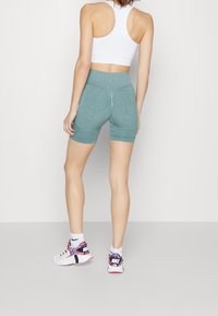 Teal idrottsshorts med texturerade paneler, figursydd design och hög midja. Kombineras med vita sneakers med färgglada detaljer.