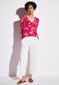 Blusa floreale rosa con scollatura a V, maniche a tre quarti, abbinata a pantaloni bianchi a gamba larga e sandali marroni senza cinturino.