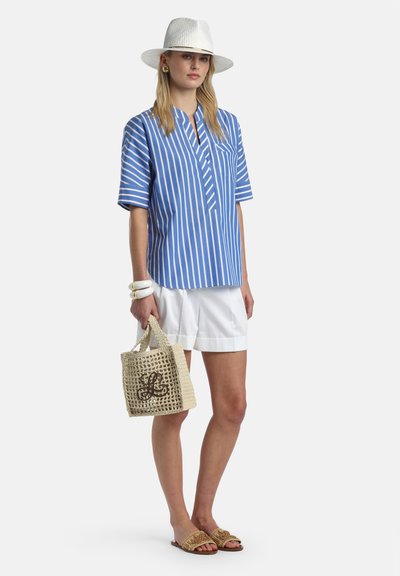 Femme portant un chapeau blanc, une chemise à manches courtes rayée bleu et blanc, un short blanc, tenant un sac tissé, portant des sandales et des bracelets.