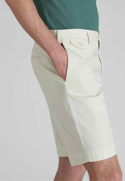 Pantaloni corti di cotone giallo chiaro con tasche laterali, caratterizzati da una vestibilità slim, una texture liscia e un orlo piegato. Chiusura semplice con bottone in vita.