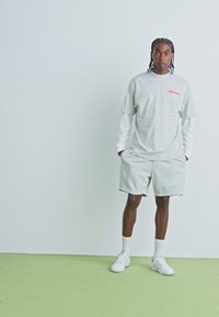 Lichtgrijs katoenen t-shirt met rode tekst, gecombineerd met bijpassende grijze shorts. Draag het met witte sneakers en sokken, tegen een effen achtergrond.