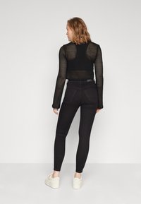 Černý zkrácený mesh top s dlouhými rukávy a texturovaným designem, spárovaný s černými skinny kalhotami s vysokým pasem a bílými teniskami.