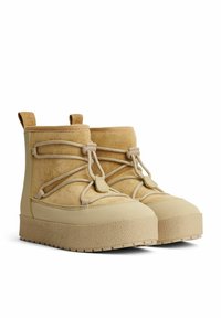 Beige ruskinds støvler med elastiske snoretræk, lav ankelhøjde, struktureret gummisål og stropper til nem påtagning. Glatte og bløde materialer.