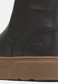 Stivale alla caviglia in pelle nera con pannelli laterali in elastico, suola in gomma e dettaglio del logo impresso sul lato esterno. Texture liscia, design minimale.