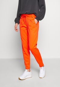 Helderoranje sweatpants met een elastische tailleband, trekkoord, zijzakken en aangesloten enkels, gedragen met witte sneakers.