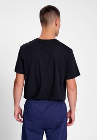 Zwart katoenen t-shirt met een ronde hals, korte mouwen en een ontspannen pasvorm, weergegeven van de achterkant. Draagt met navy elastische taillebandbroek.