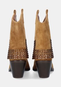 Botas de tobillo de ante en color marrón claro con puntera redondeada, adornadas con tachuelas metálicas a lo largo de los lados y un tacón de bloque.