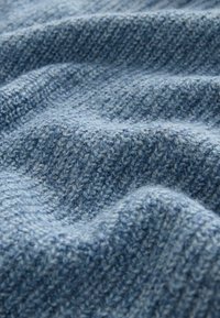 Mīksts zils audums ar teksturētu aušanu, kas satur dažādas zila toņu nianses un vieglas viļņošanās, kas norāda uz dziļumu un siltumu.