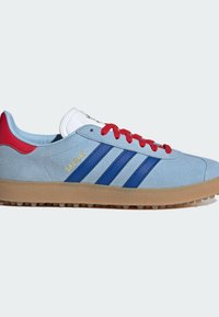 Baskets en suède bleu clair avec semelle en gomme, lacets rouges et trois rayures bleues. Présente une languette blanche avec le logo de la marque et le détail "GAZELLE".