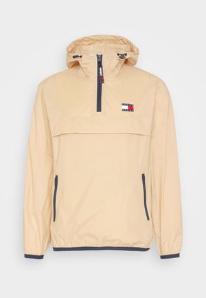 Beige Tommy Jeans windjack met capuchon, vooraan een halve rits, twee zijzakken met rits, verstelbare capuchon en logo-opdruk op de borst.