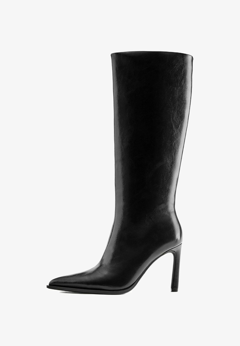 Bottes en cuir noir montantes jusqu’au genou avec talon haut, bout pointu et talon aiguille fin, vues de côté sur fond blanc.