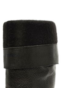 Bota de cuero negro con un acabado texturizado, con un borde de piel de pelo negro ancho y una correa de cuero suave que acentúa la parte superior.