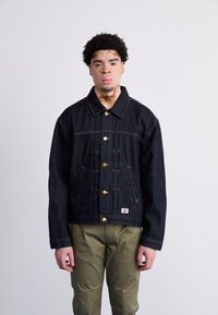 Giacca di denim scuro con colletto, bottoni dorati e cuciture a contrasto. Presenta due tasche inferiori e un design cropped.