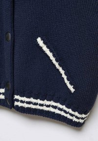 Marineblauer Strickcardigan mit einem weißen diagonalem Streifen auf der Tasche, schwarzen Knöpfen und kontrastierenden gestreiften Akzenten am Saum.