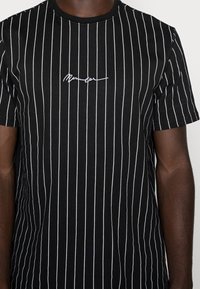 Černé tričko s krátkým rukávem, s vertikálními bílými pruhy a malým vyšitým bílým logem na hrudi. Bavlněný materiál, přiléhavý střih.