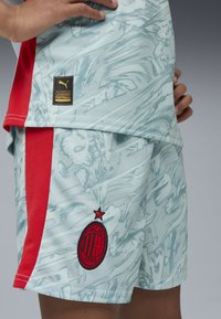 Jasnoniebieskie szorty sportowe z teksturowanym wzorem, czerwonymi akcentami po bokach oraz czarnym logo AC Milan z czerwoną gwiazdką. Zawierają czarną metkę Puma.