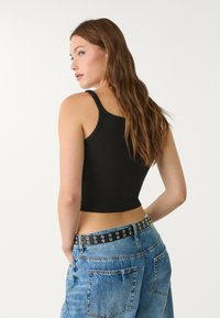 Débardeur noir ajusté avec des bretelles fines, associé à un jean taille haute bleu clair, arborant une ceinture noire avec des œillets en argent.