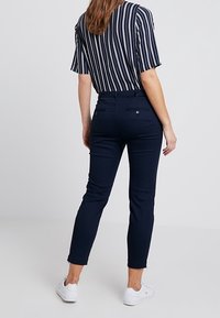 Mörkblå figurnära byxor med en jämn textur, medelhög midja och två bakfickor. Matchas med en randig topp med avslappnad passform.