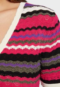 Knit sweater featuring a V-neck design with multicolored zigzag stripes in pink, black, purple, white, and olive green. Textured open weave.